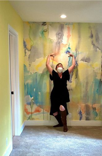 A woman wearing a mask is standing in front of a painting on the wall.