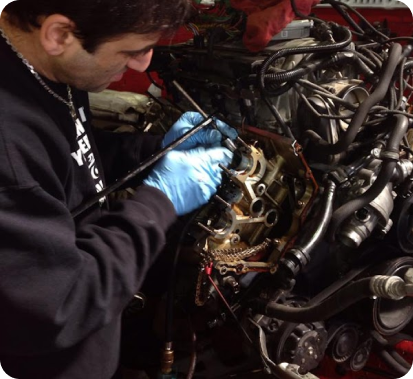 Mechanic in blue gloves working on a car engine with exposed wires and parts | Universal Auto Repair