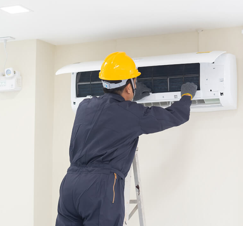 A man wearing a hard hat is working on an air conditioner.