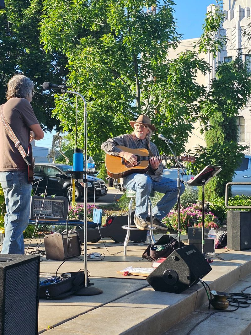 A man is playing a guitar on a stage in a park.