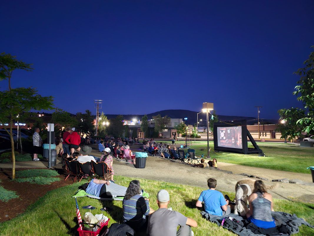 A group of people are sitting in the grass watching a movie.