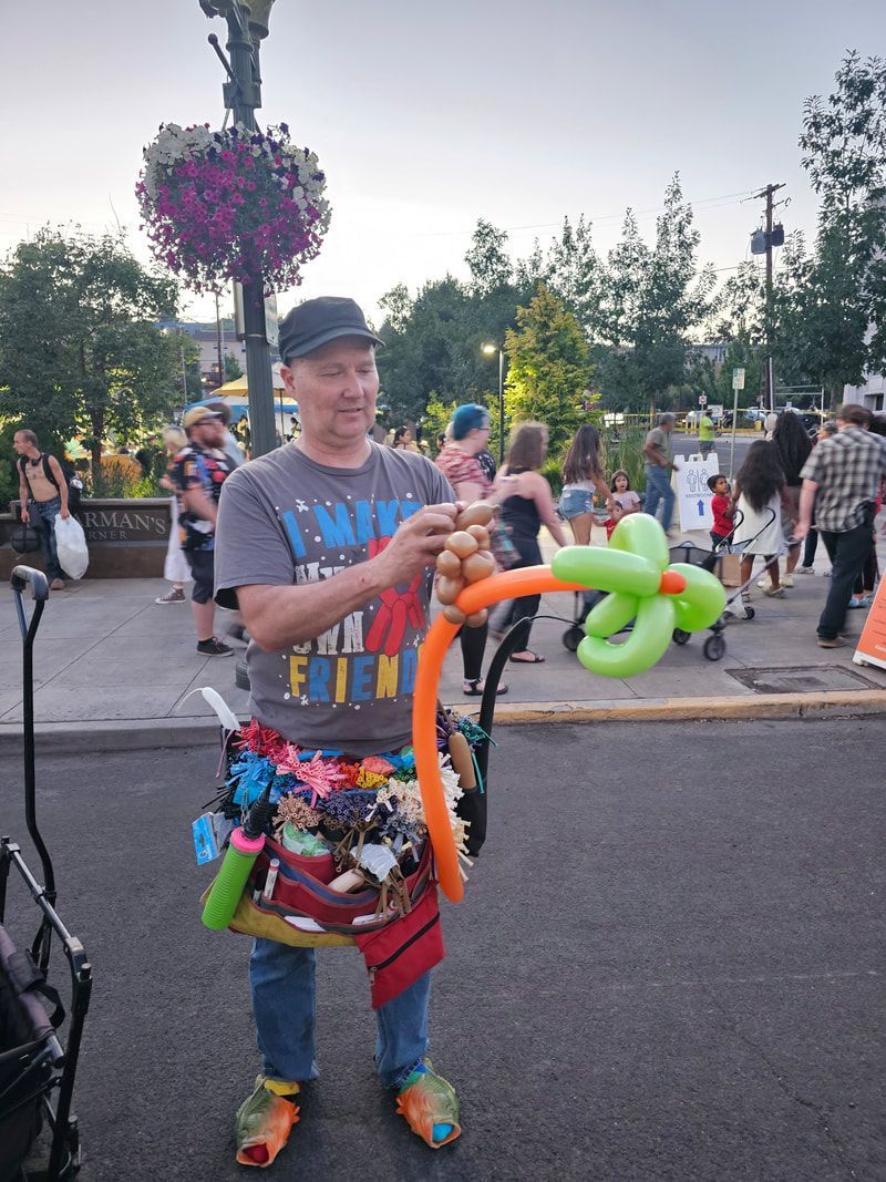 A man is standing on the side of the road holding balloons.