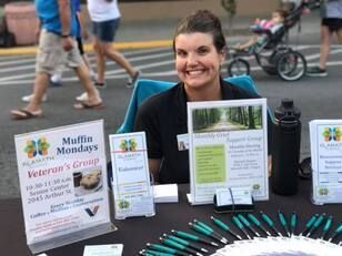 A woman is sitting at a table with a sign that says muffin mondays.