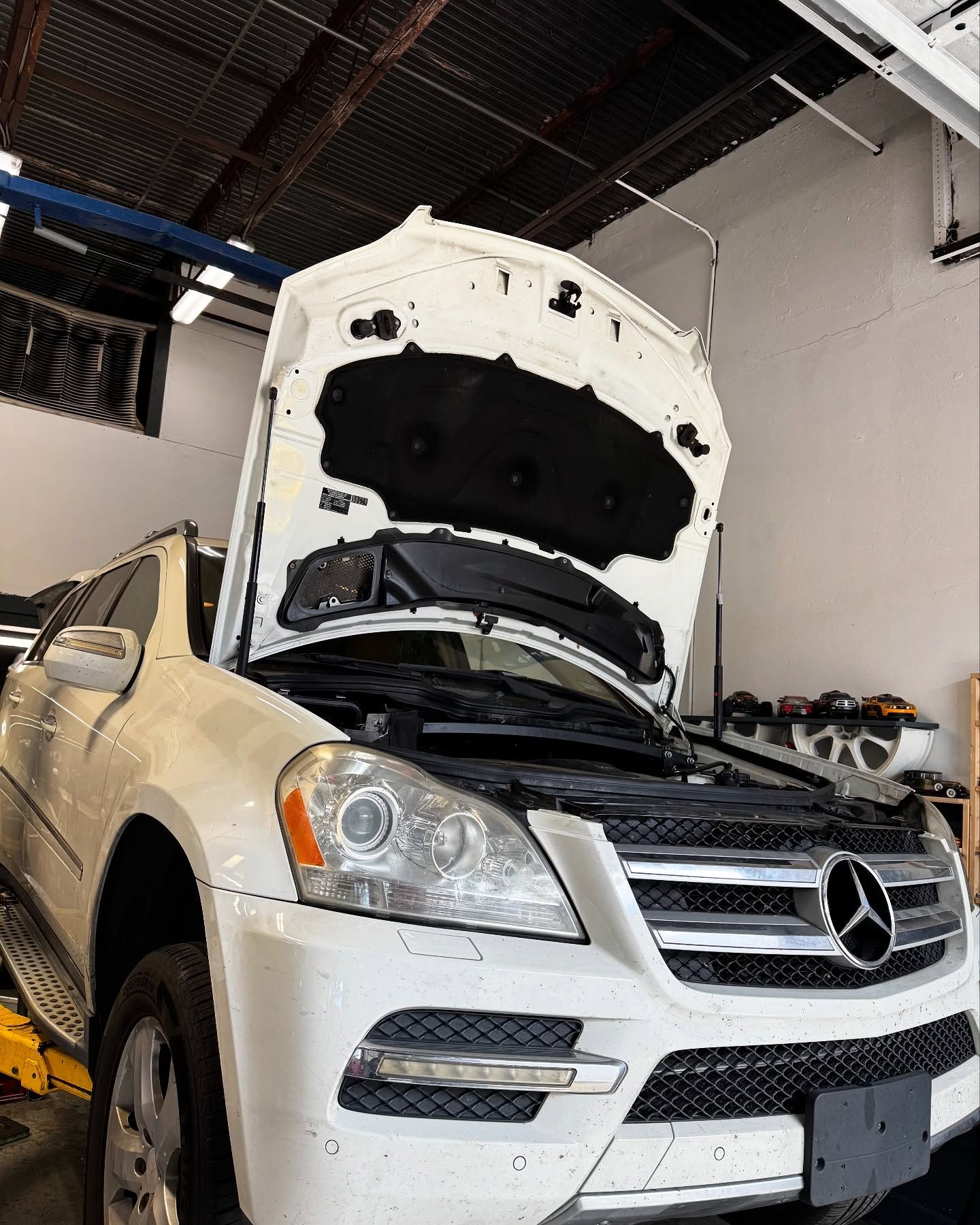 White Mercedes SUV with the hood open in a repair shop.