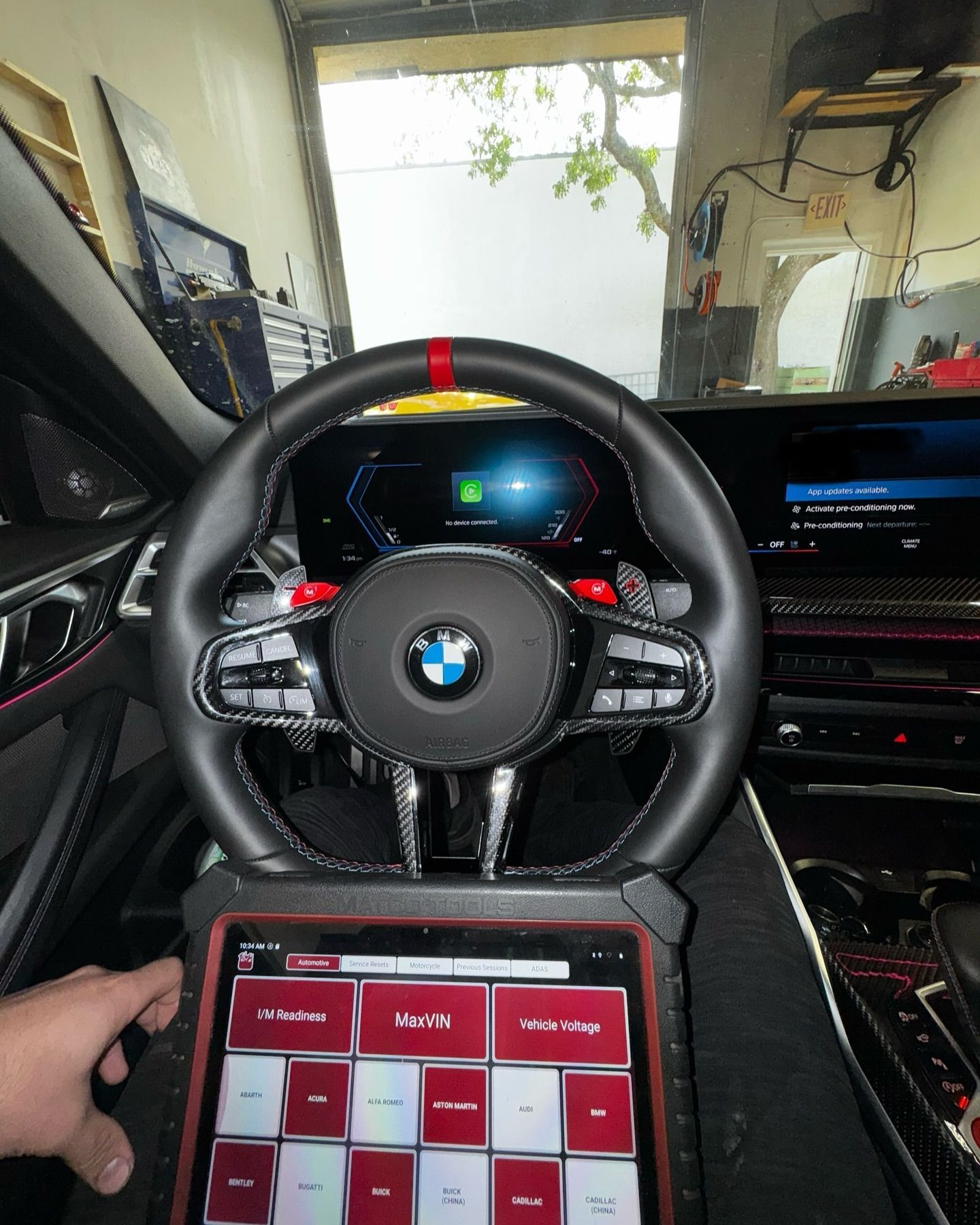 Car interior with a steering wheel, diagnostic tablet, and driver's hands.