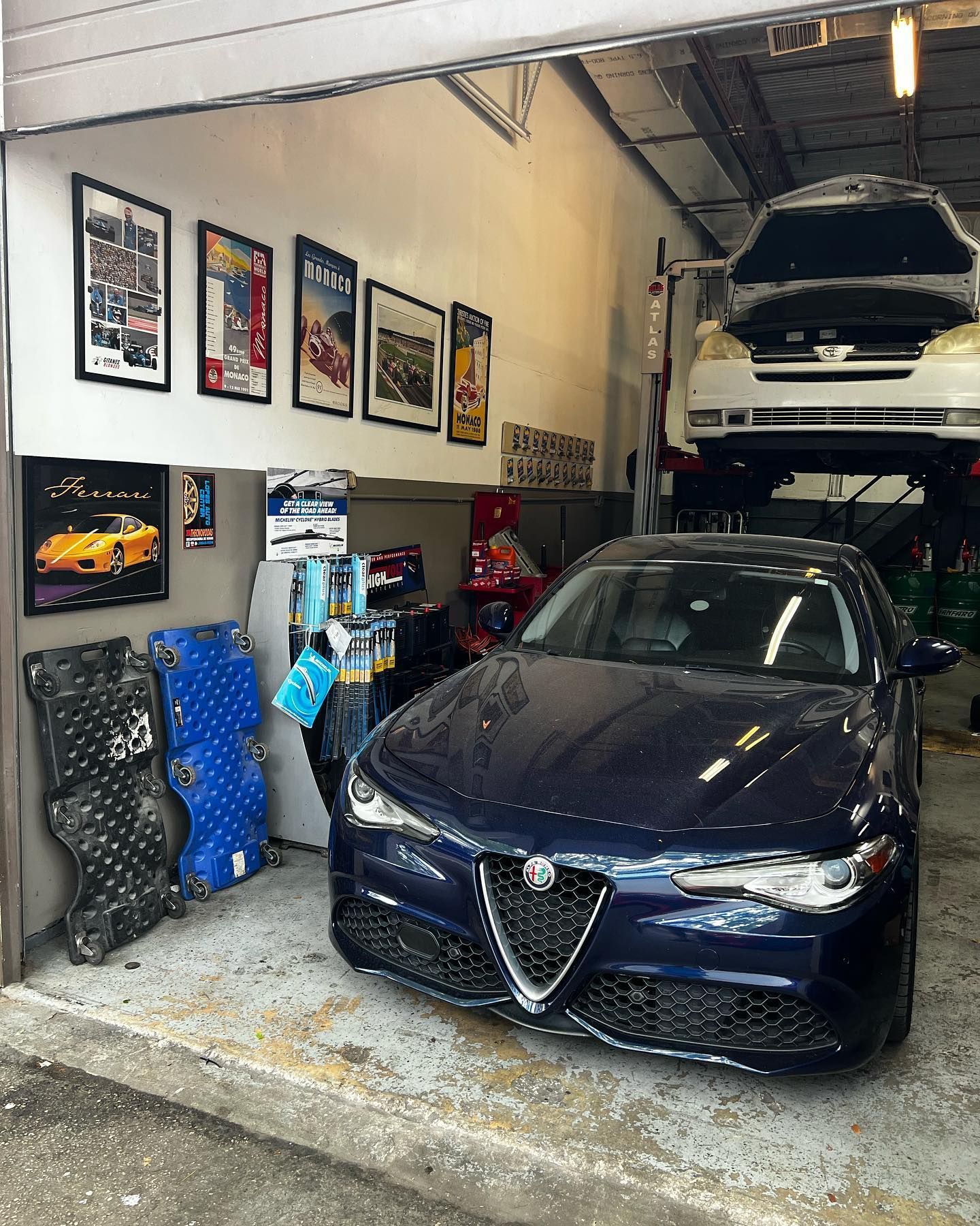 Dark blue Alfa Romeo sedan parked in a garage with a car raised on a lift.