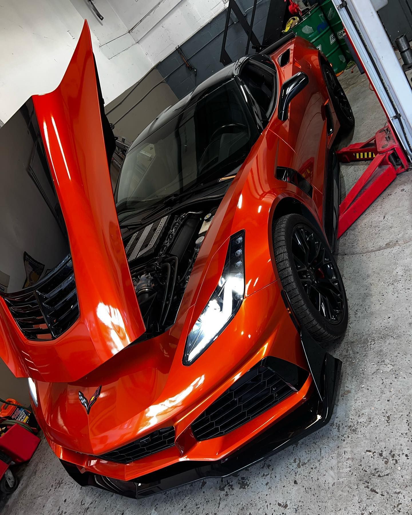 Black BMW M4 with hood open, carbon fiber splitter, in a garage setting.