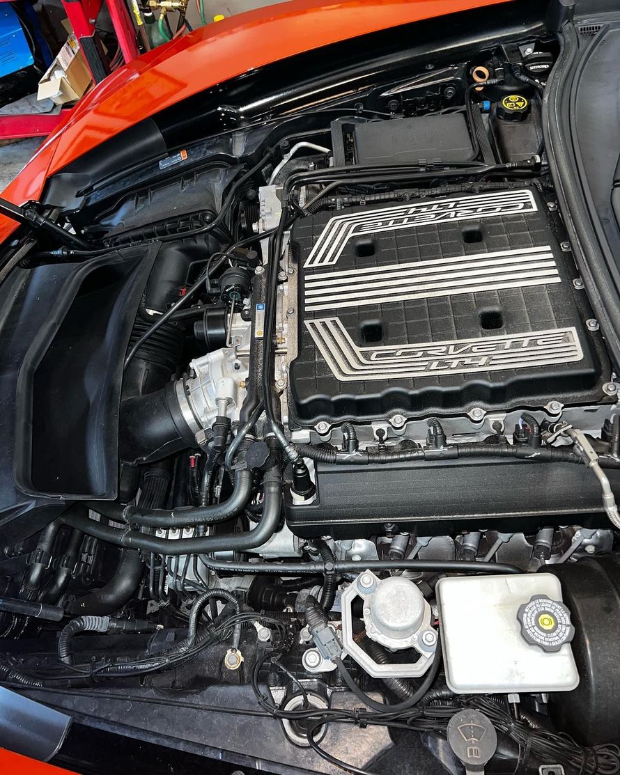 Orange sports car engine bay with black supercharger.
