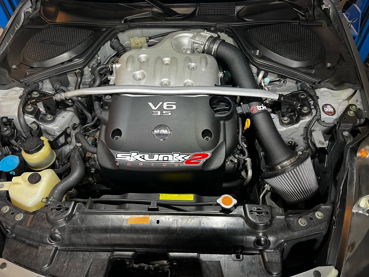 Black BMW M4 with hood open, carbon fiber splitter, in a garage setting.