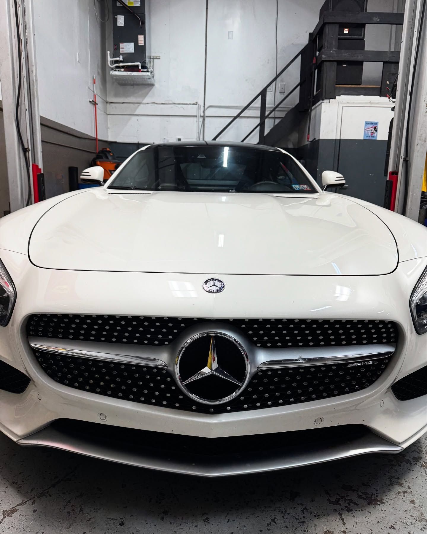 White Mercedes-AMG GT sports car in a garage. Black grill with Mercedes logo.