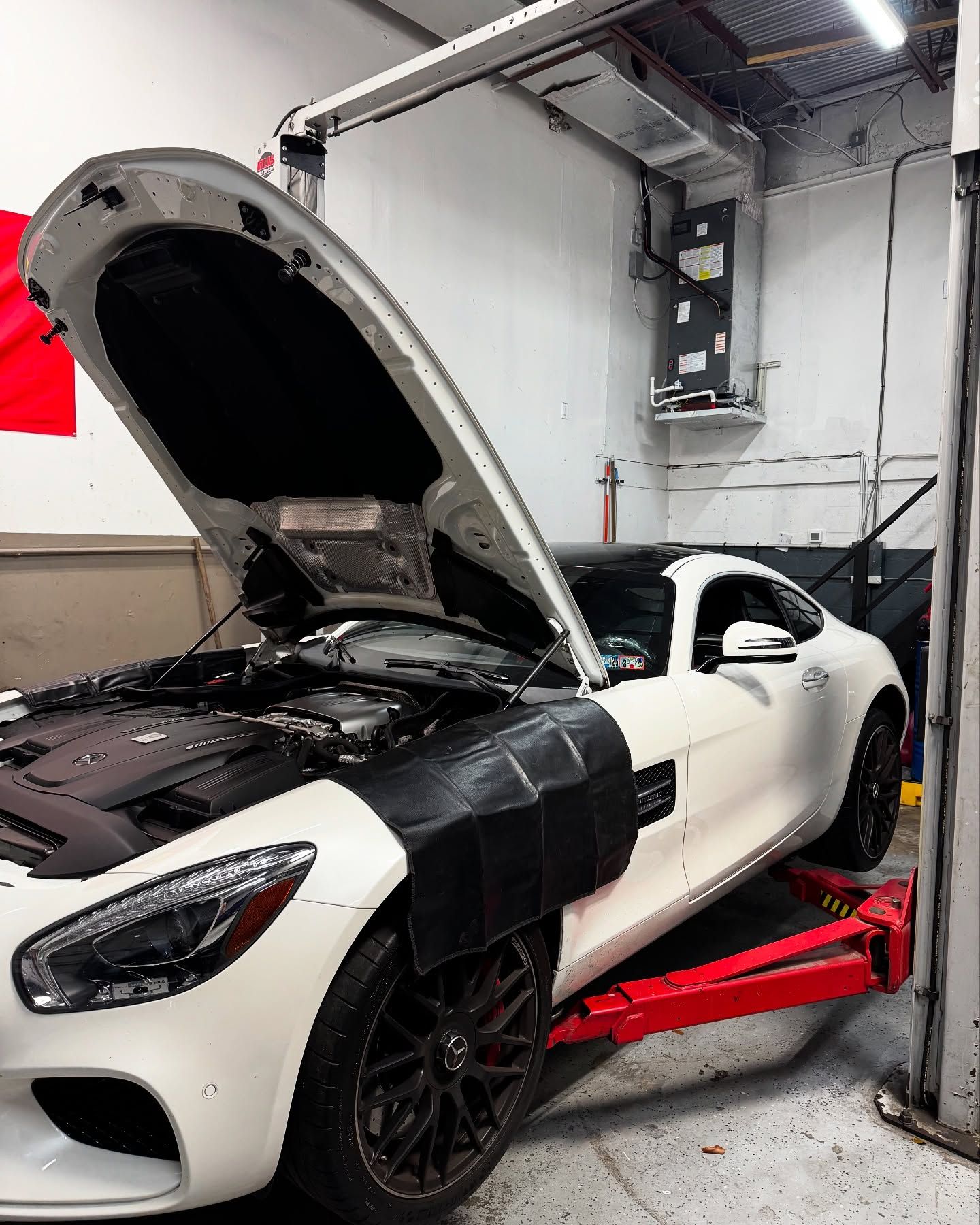 White sports car on a lift with the hood open in an auto repair shop.