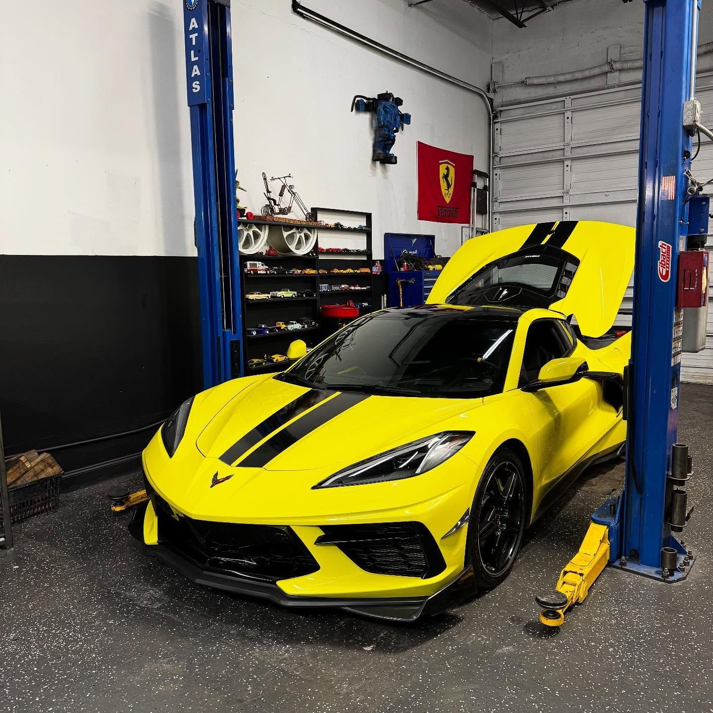 Yellow Corvette sports car on a lift in a garage with its hood open.