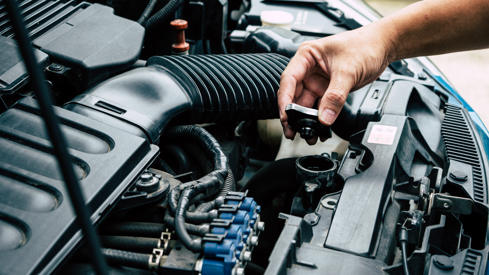 A person's hand opening the radiator cap in a car engine, checking the cooling system.