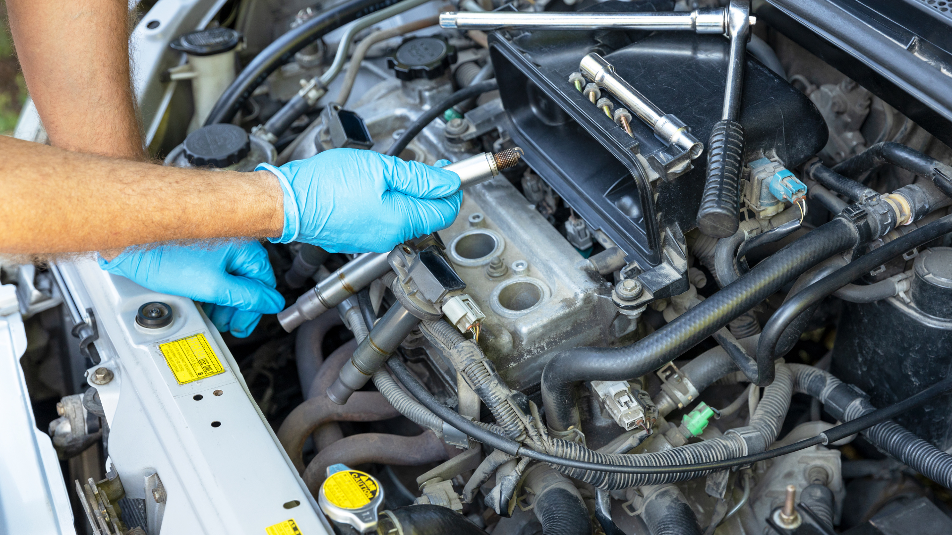 Mechanic in gloves working on a car engine with a wrench in a garage.