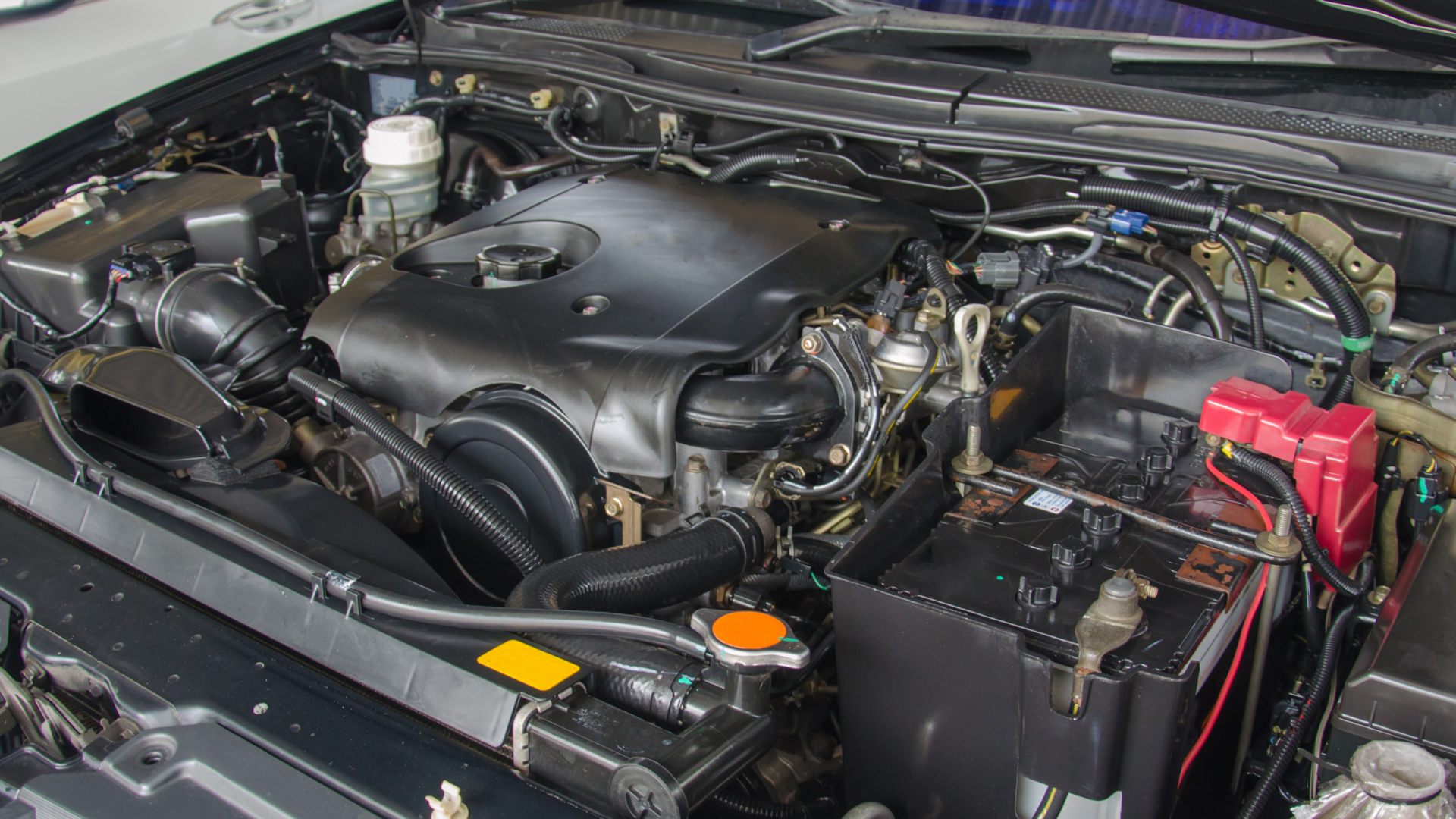 Mechanic working on a car engine in a garage, wearing gloves and using a wrench.
