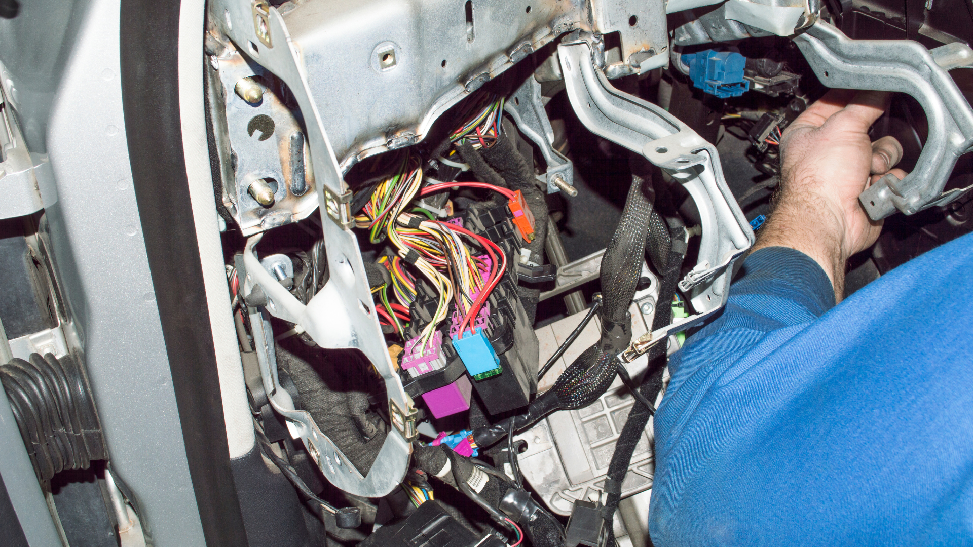 Person cleaning a shiny black car engine bay with an air hose in a garage.