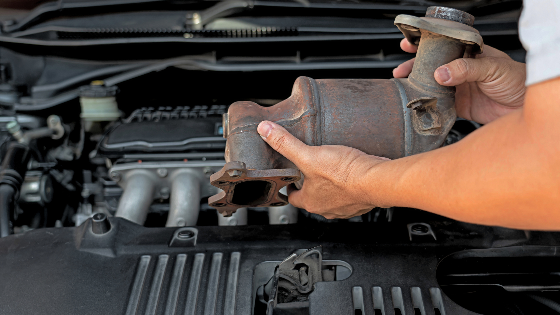 Mechanic working on a car engine in a garage, wearing gloves and using a wrench.