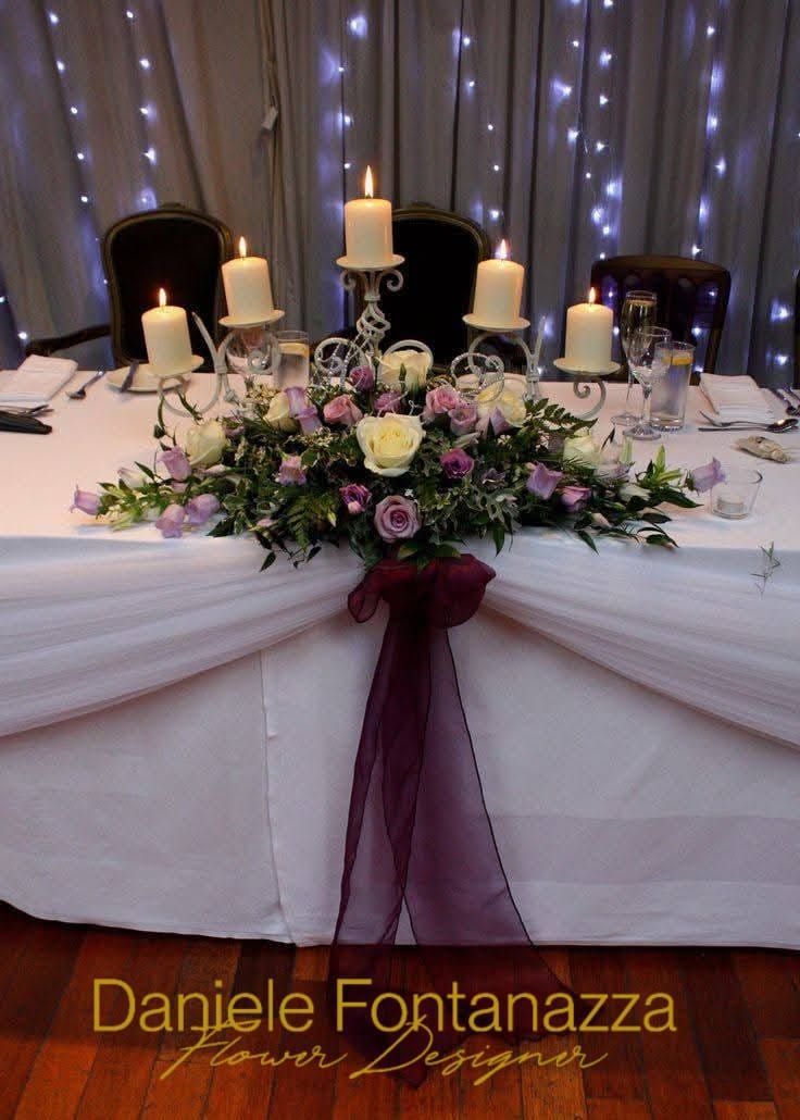 Centrotavola per matrimonio con candele, fiori e tessuto drappeggiato; nastro bordeaux.