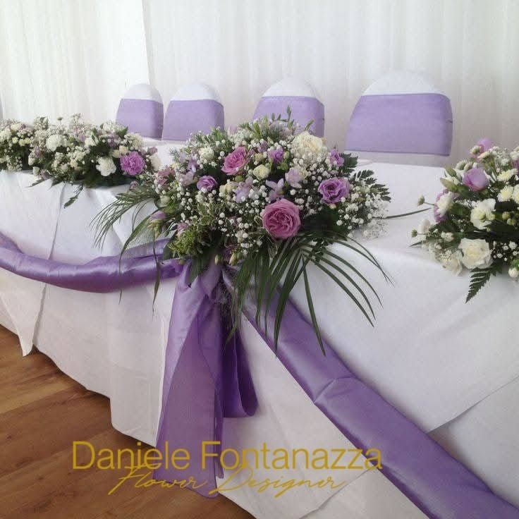 Tavolo principale per matrimonio con composizioni floreali e drappeggi color lavanda e bianchi.