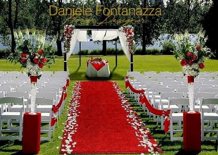 Allestimento per la cerimonia nuziale con tappeto rosso, sedie bianche, composizioni floreali e baldacchino in un parco.