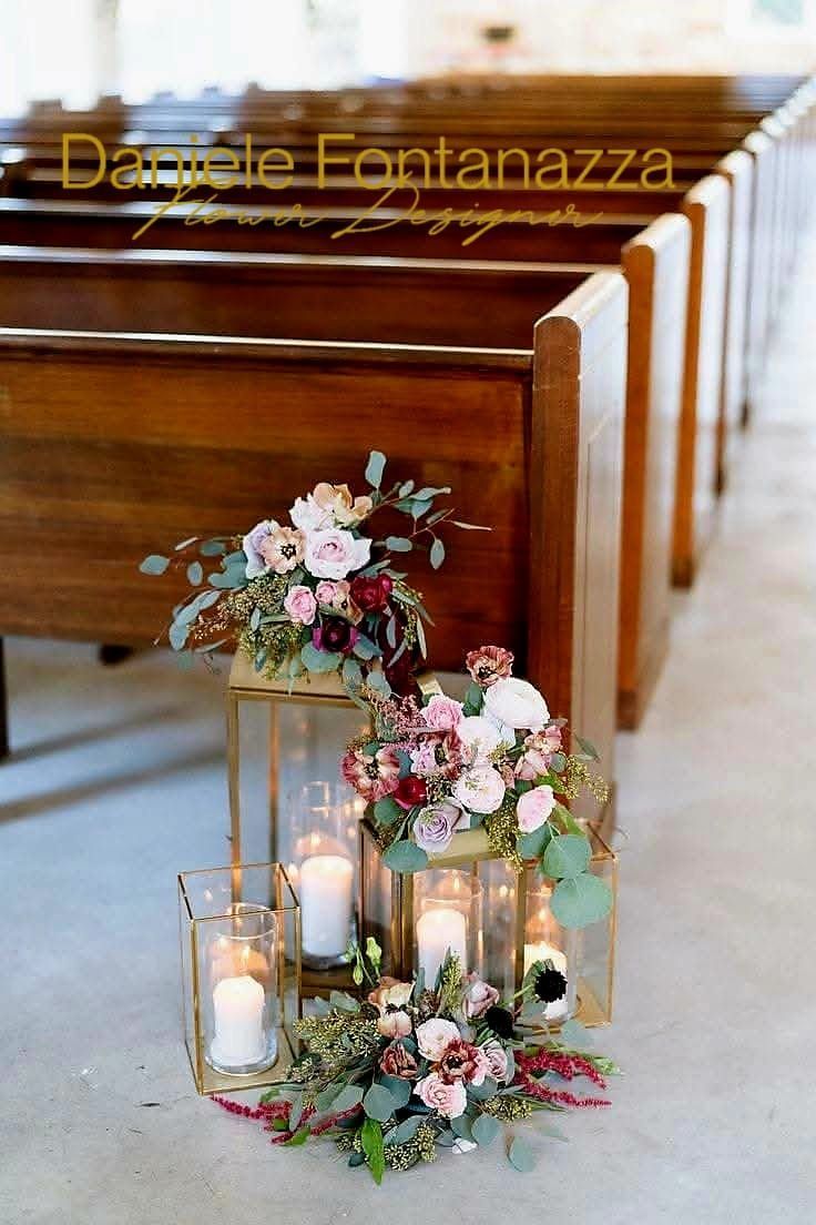 Navata della chiesa decorata con composizioni floreali e candele. Panche di legno fiancheggiano i lati.