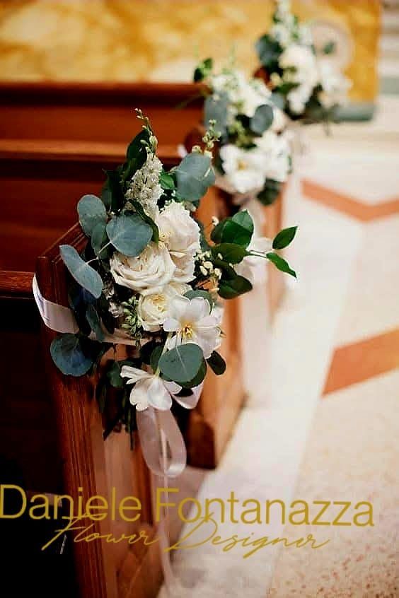 Mazzi di fiori bianchi con eucalipto legati ai banchi della chiesa con nastri.