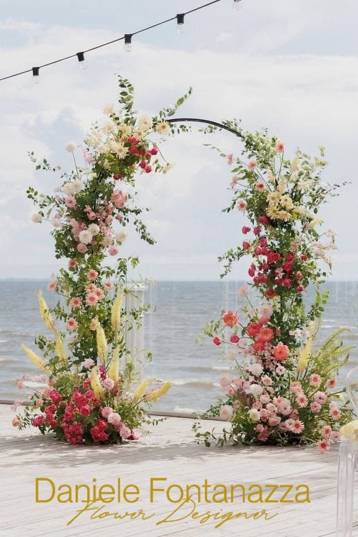 Arco floreale con fiori rosa, rossi e gialli, con vista sull'oceano. Testo