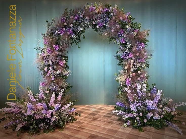 Arco floreale decorato con fiori di lavanda e bianchi, con composizioni abbinate alla base.