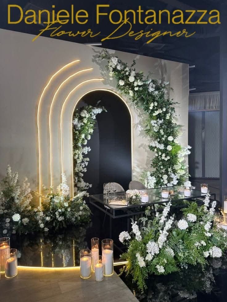 Elegante composizione floreale con arco sullo sfondo per un evento. Fiori bianchi, candele e luci al neon.