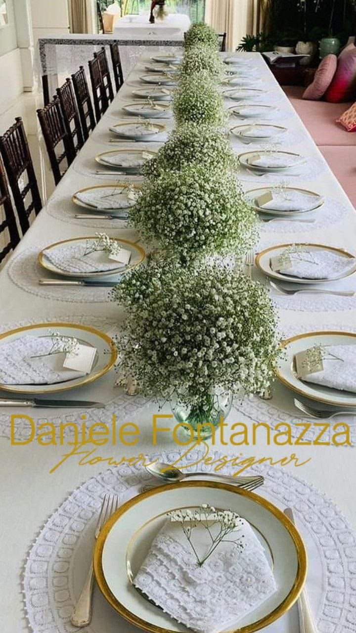 Lungo tavolo da pranzo apparecchiato per un evento formale, decorato con centrotavola floreali di gypsophila.