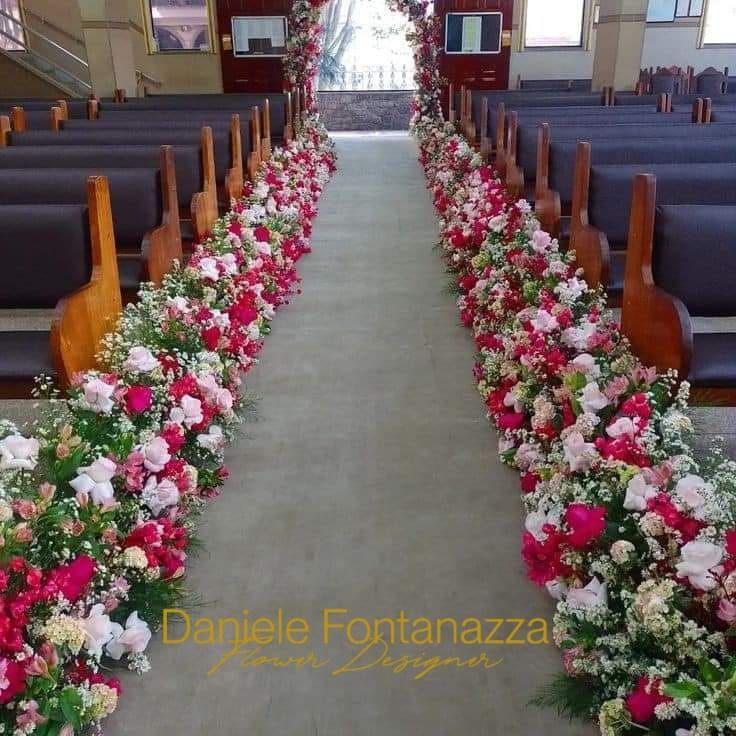Navata della chiesa decorata con fiori rossi e bianchi per una cerimonia.