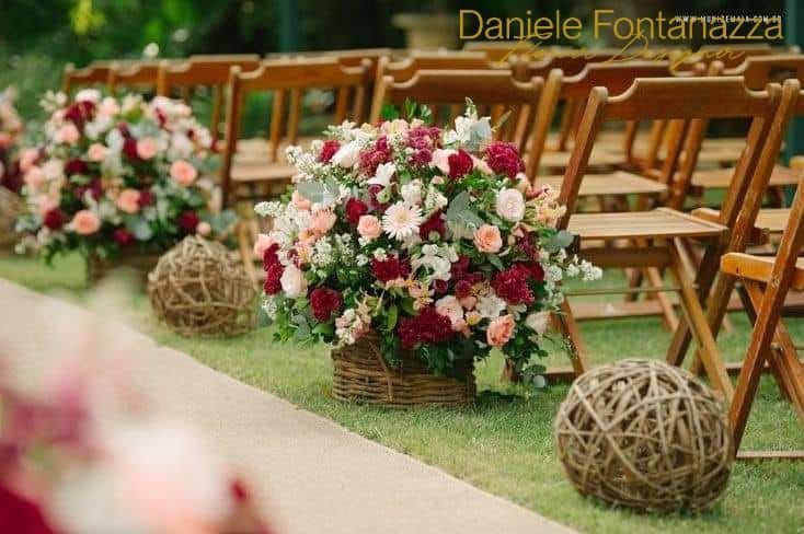 Decorazioni per la cerimonia nuziale: composizioni floreali in cestini, sedie in legno e palline di spago decorative sull'erba.