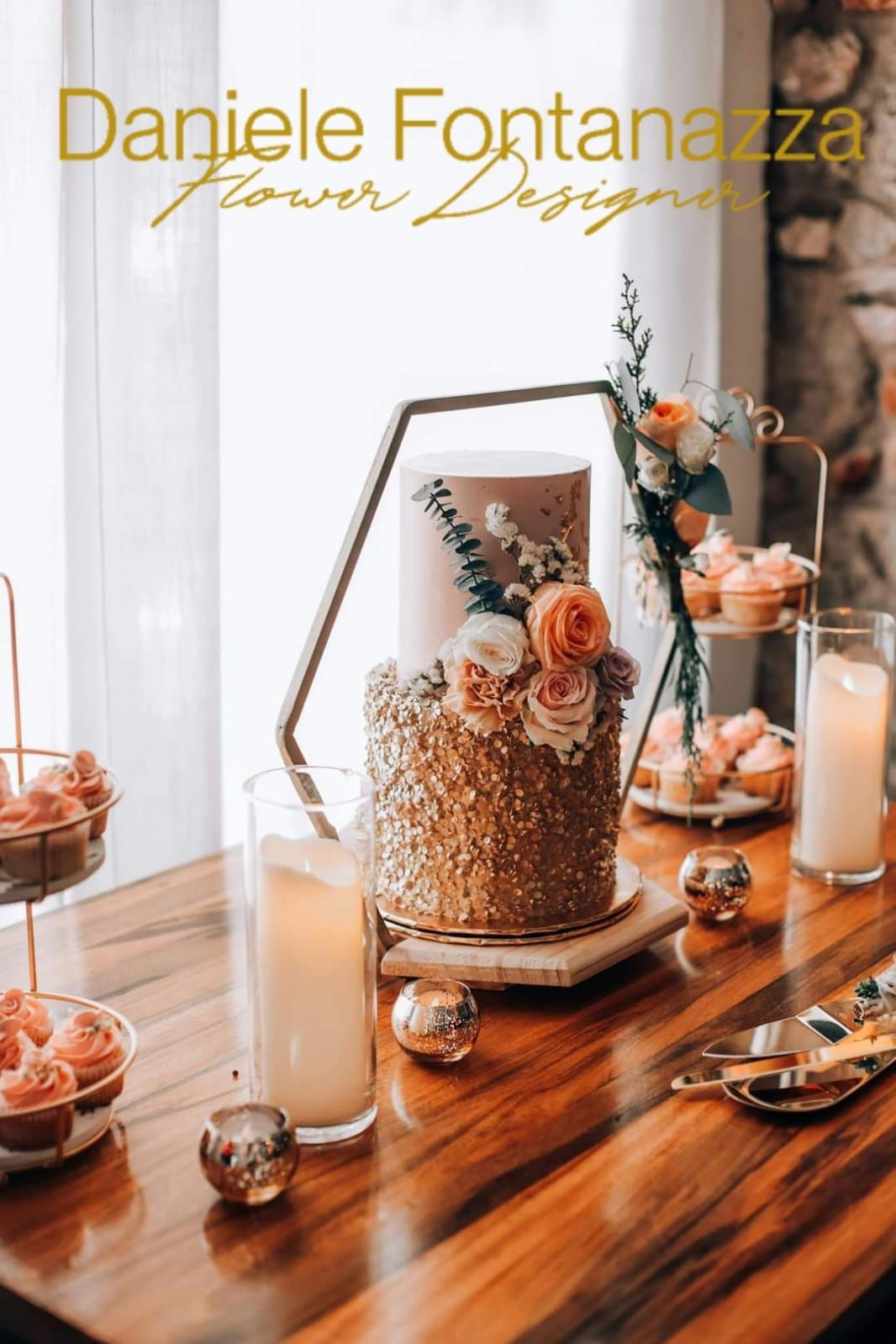 Torta con paillettes dorate, fiori, dolci, candele e una bevanda su un tavolo di legno.