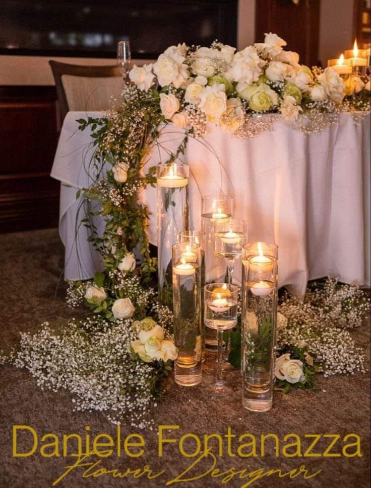 Tavolo del ricevimento nuziale con rose bianche, gypsophila e candele galleggianti.