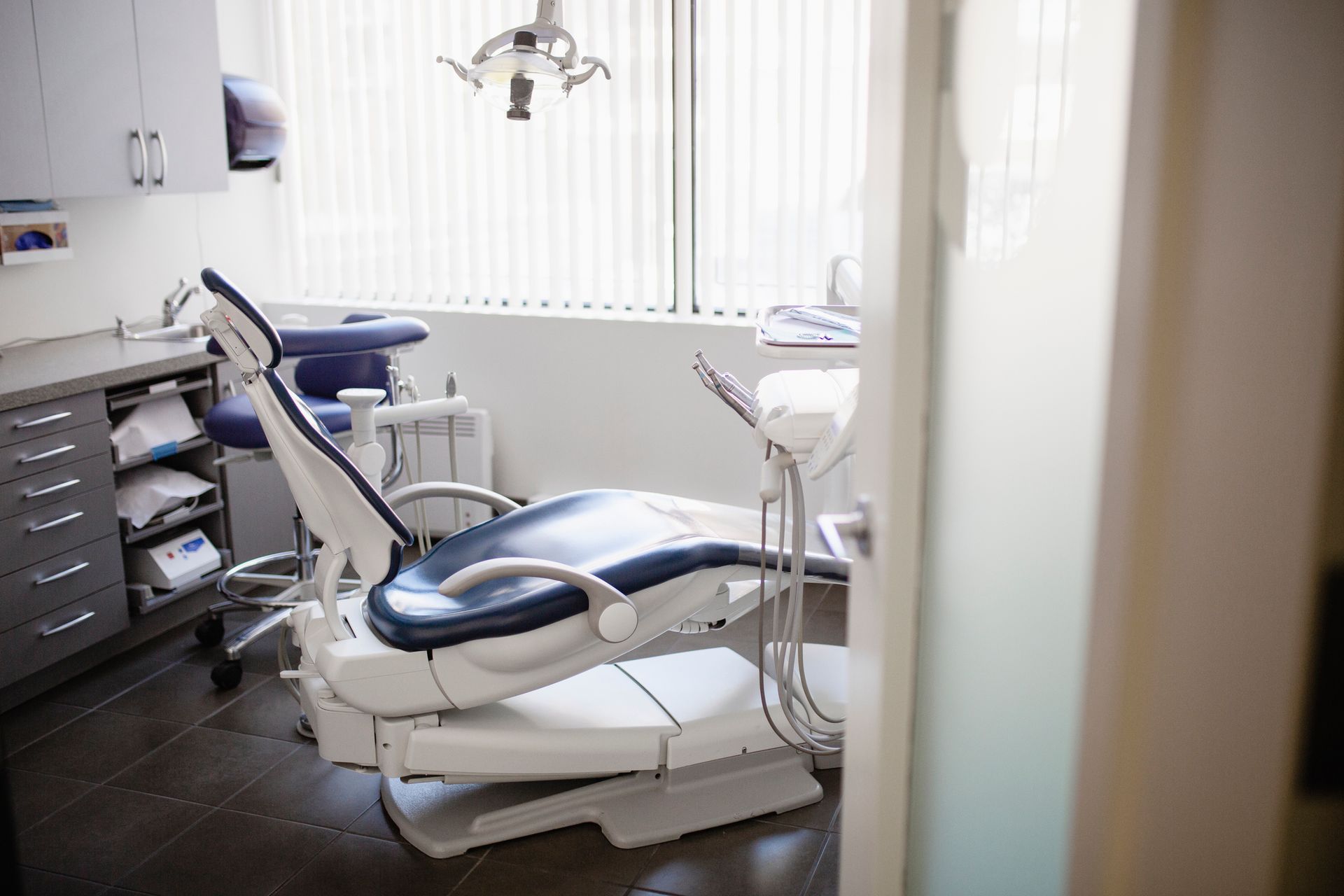 Dental chair in a modern, bright office. The room has a window, cabinets, and dental equipment.