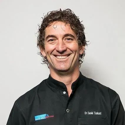 Smiling Dr. Daniel Tankard, dark curly hair, black top, white background.