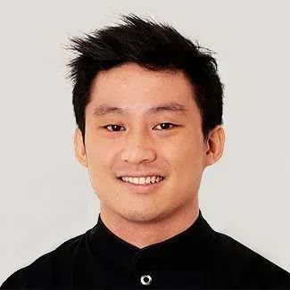Smiling Asian man with short black hair, wearing a black shirt against a plain background.