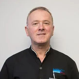Middle-aged man in black collared shirt with a name tag, smiling at the camera.