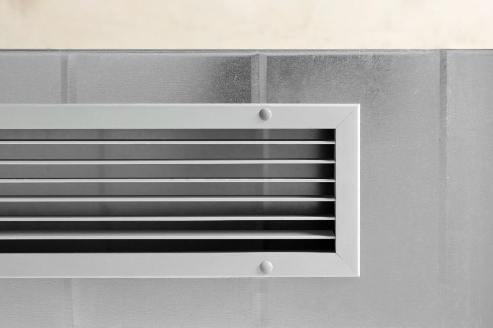 A close up of a white air vent on a gray wall.