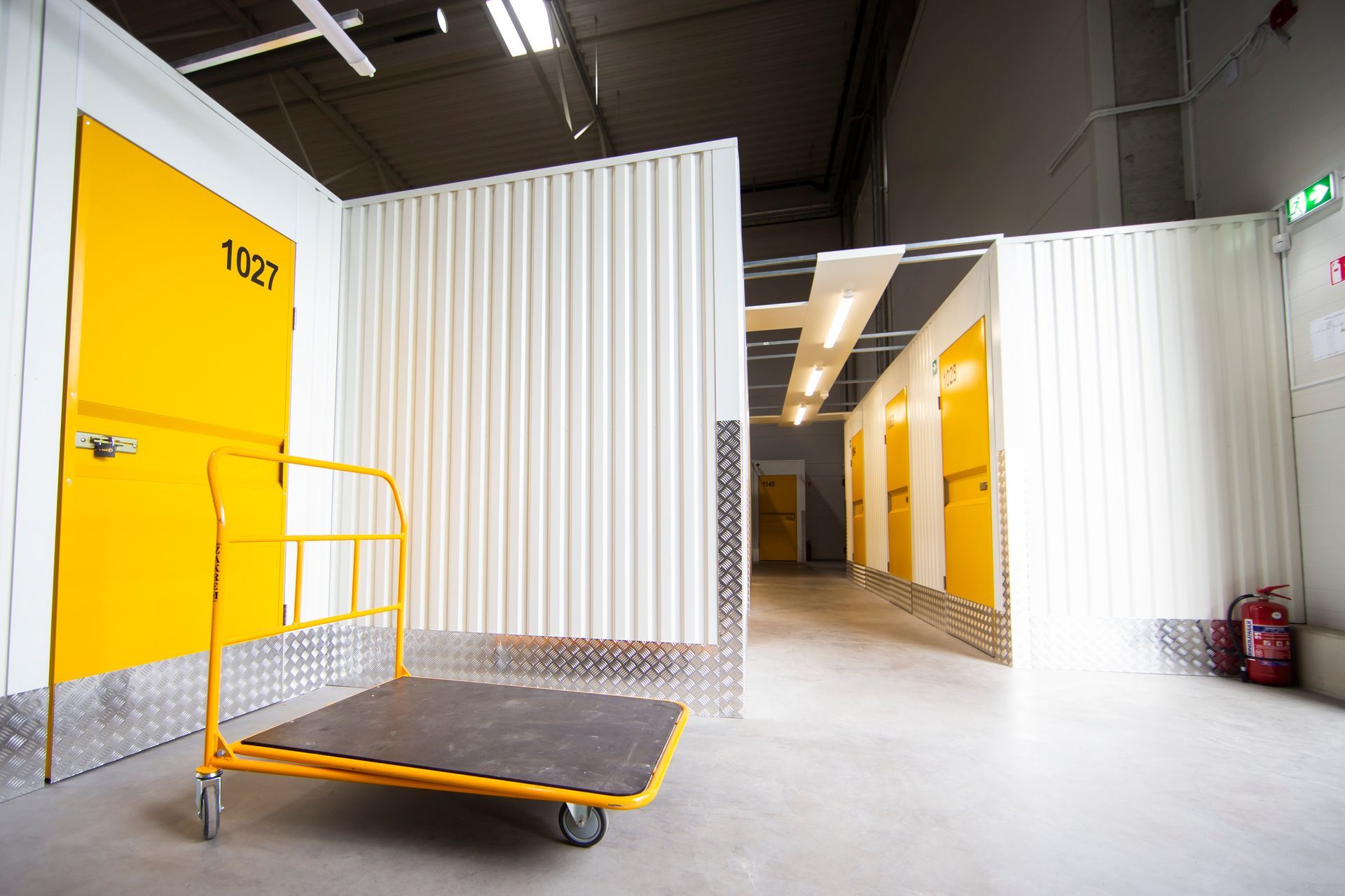Indoor self-storage facility hallway with yellow unit doors and a rolling cart in the foreground. Indoor self-storage facility hallway with yellow unit doors and a rolling cart in the foreground.