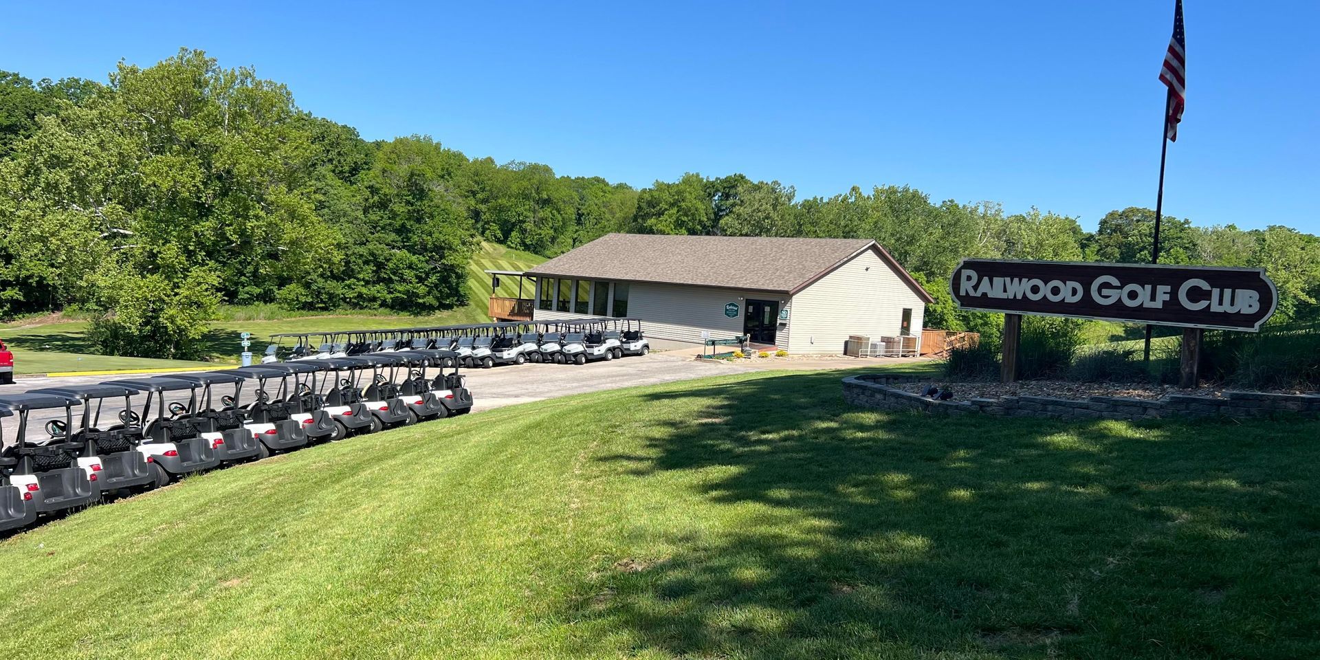 Rambow Golf Club entrance with parked golf carts, clubhouse, and American flag on a sunny day