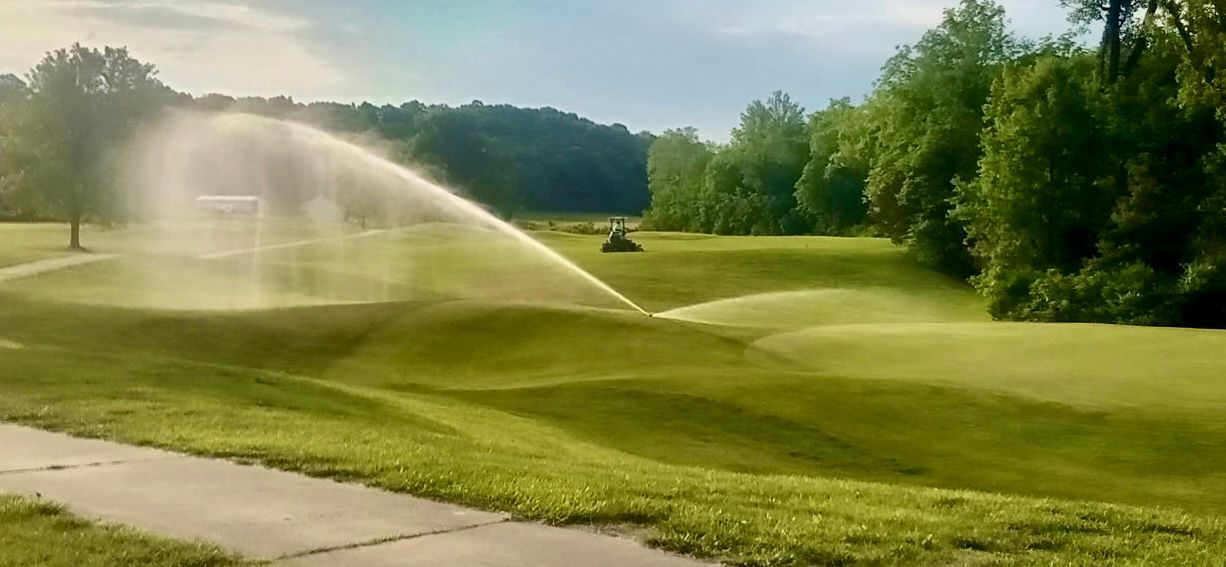 Sprinklers watering a lush green golf course under a clear sky