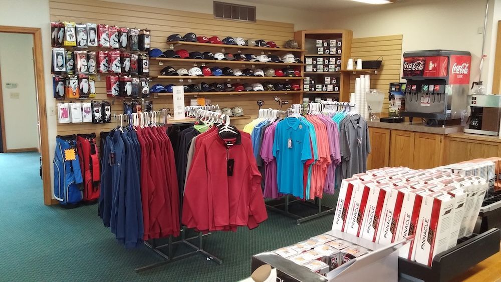 Retail clothing store interior with racks of shirts and jackets, shelves of merchandise, and a Coca-Cola cooler