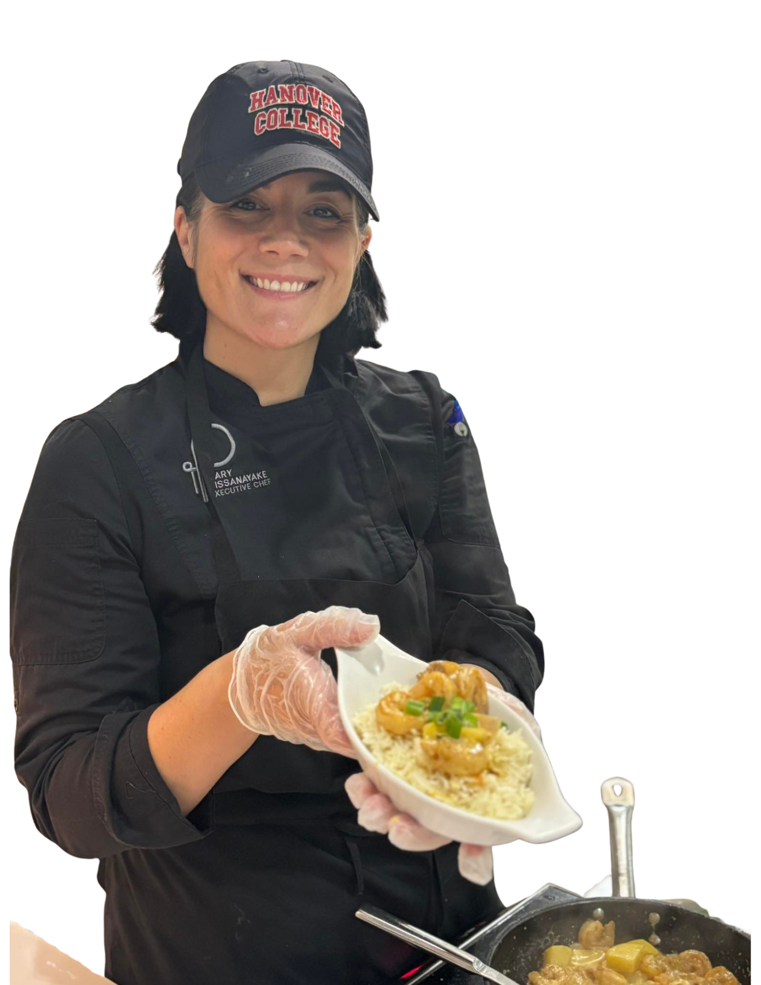 Chef holding a bowl of food, smiling. She wears a black chef's jacket and cap. Food in bowl appears to be curry with shrimp on top of rice.