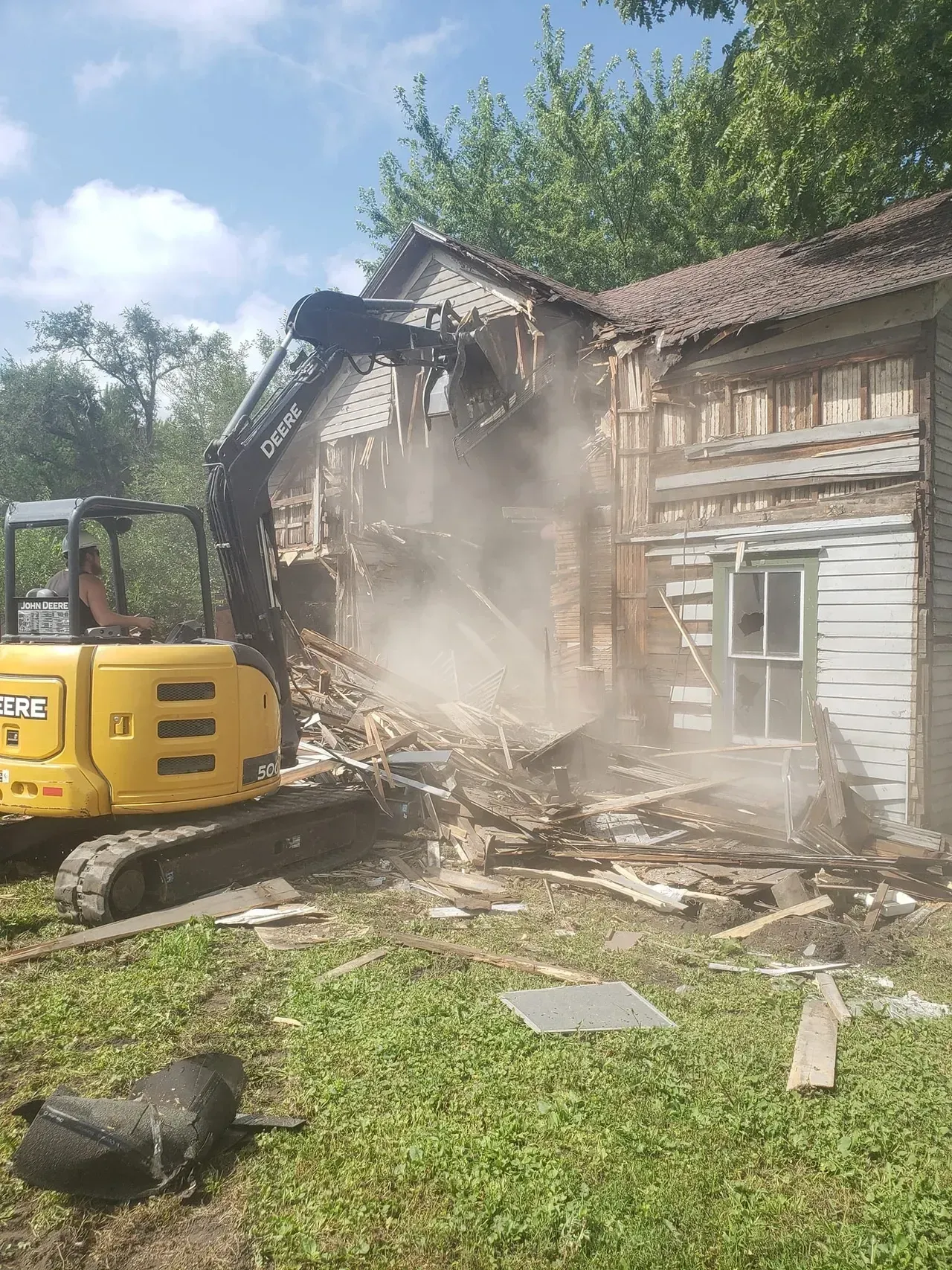 A yellow excavator is demolishing a house in a backyard.