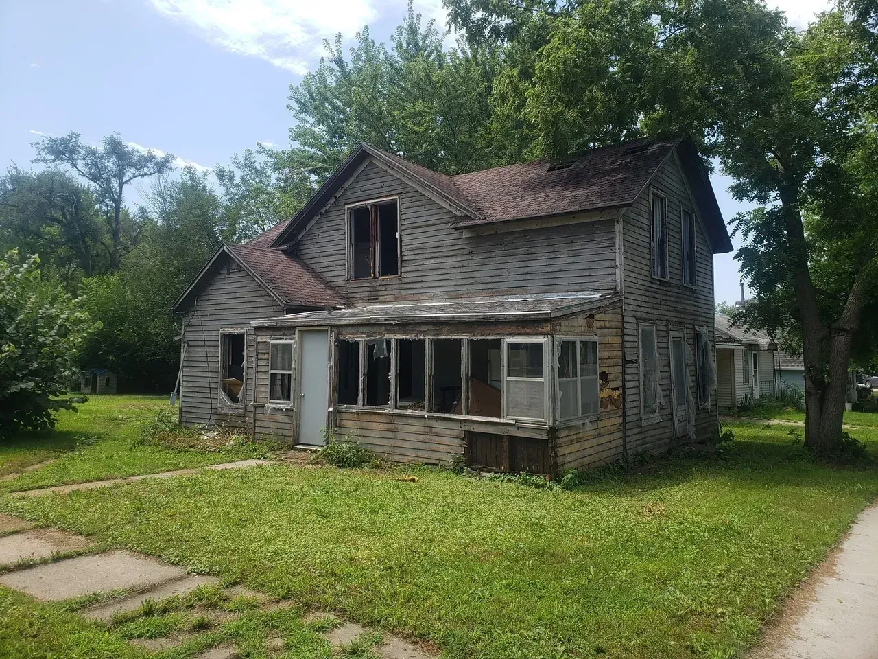 An old abandoned house is sitting in the middle of a grassy field.