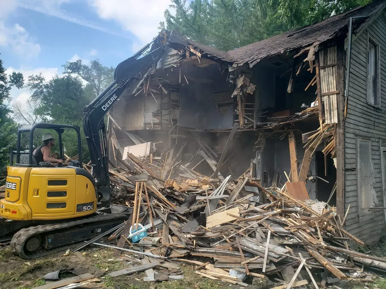 A yellow excavator is demolishing a house.