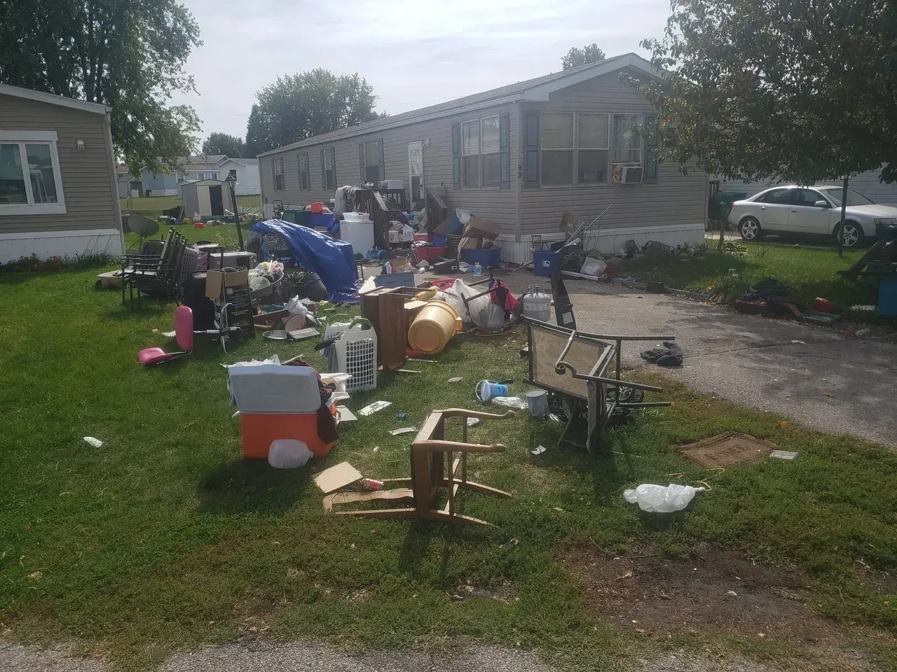 There is a lot of trash in the grass in front of a mobile home.