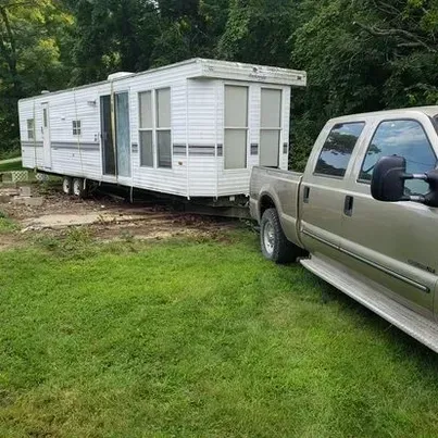 A truck is towing a trailer in a grassy field.