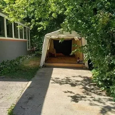 A white tent is sitting in a driveway next to a house.